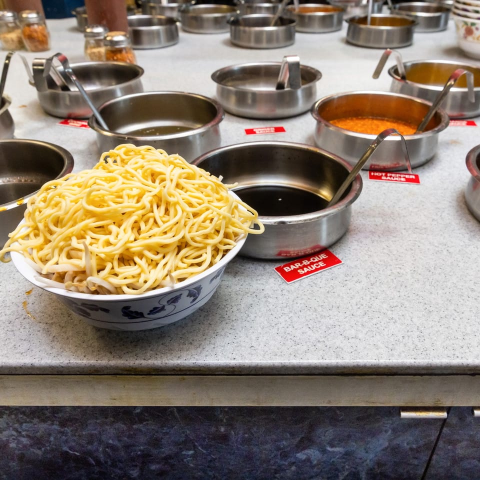 A buffet line with bowls of noodles, sauces, and spices at Hi Ho Mongolian Grill.